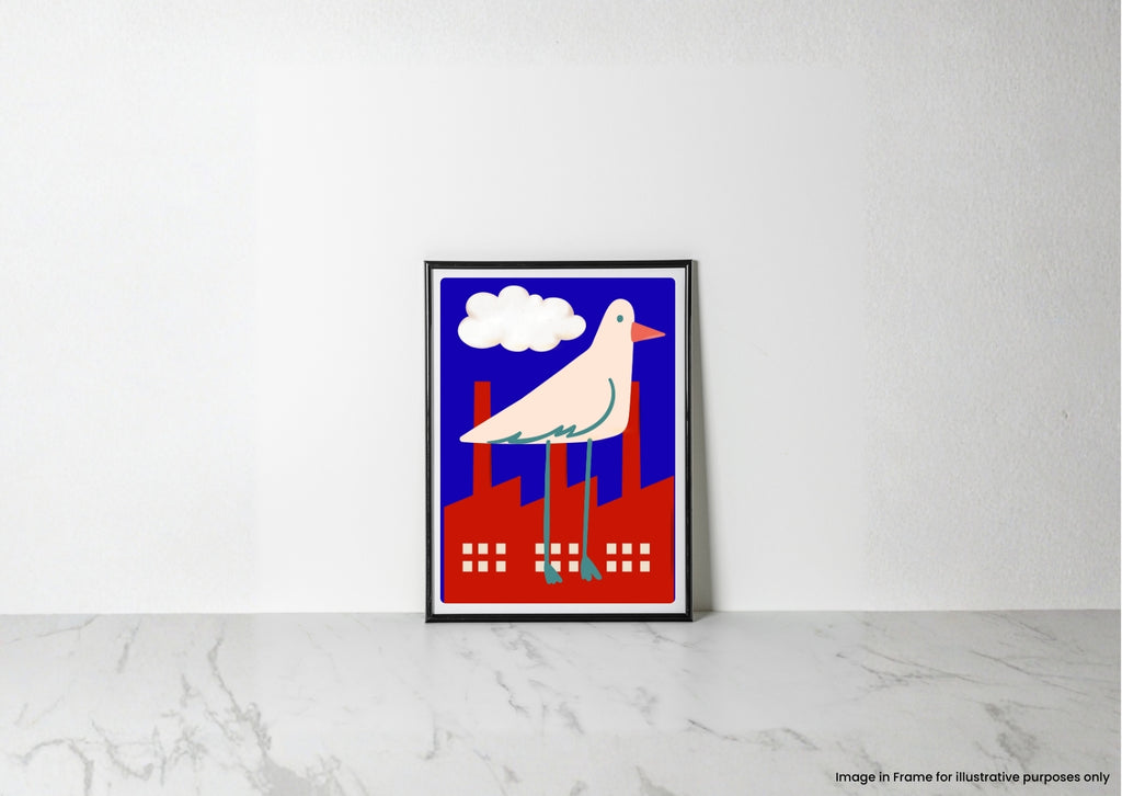 A framed art print featuring a stylized white bird with a pink beak standing on red factory chimneys under a blue sky with a white cloud, leaning against a white wall on a light marble surface.
