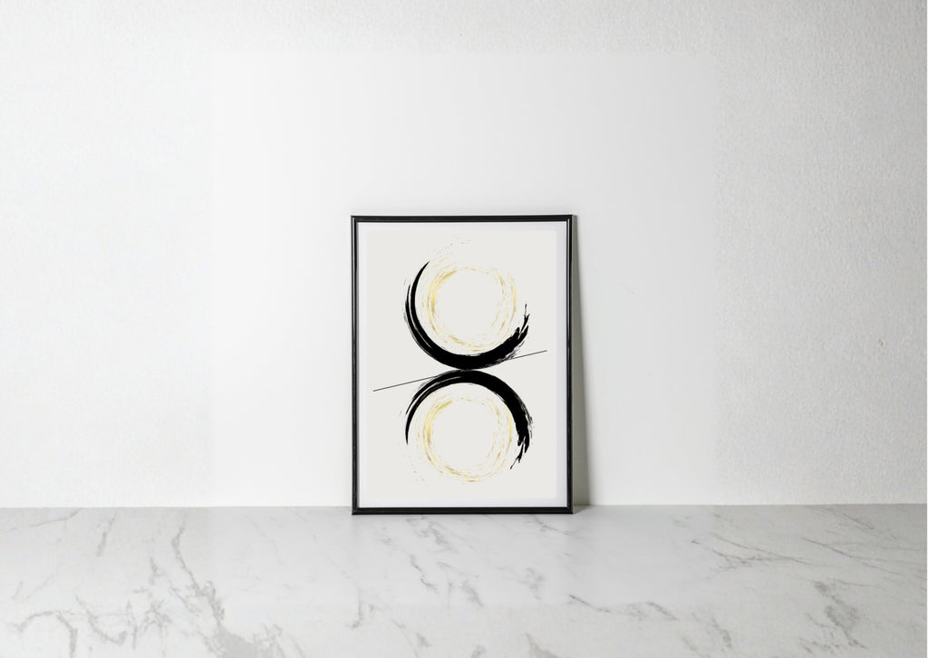 A minimalist framed art print featuring a black and gold abstract circular design on a white background, leaning against a white wall on a light gray marble surface.