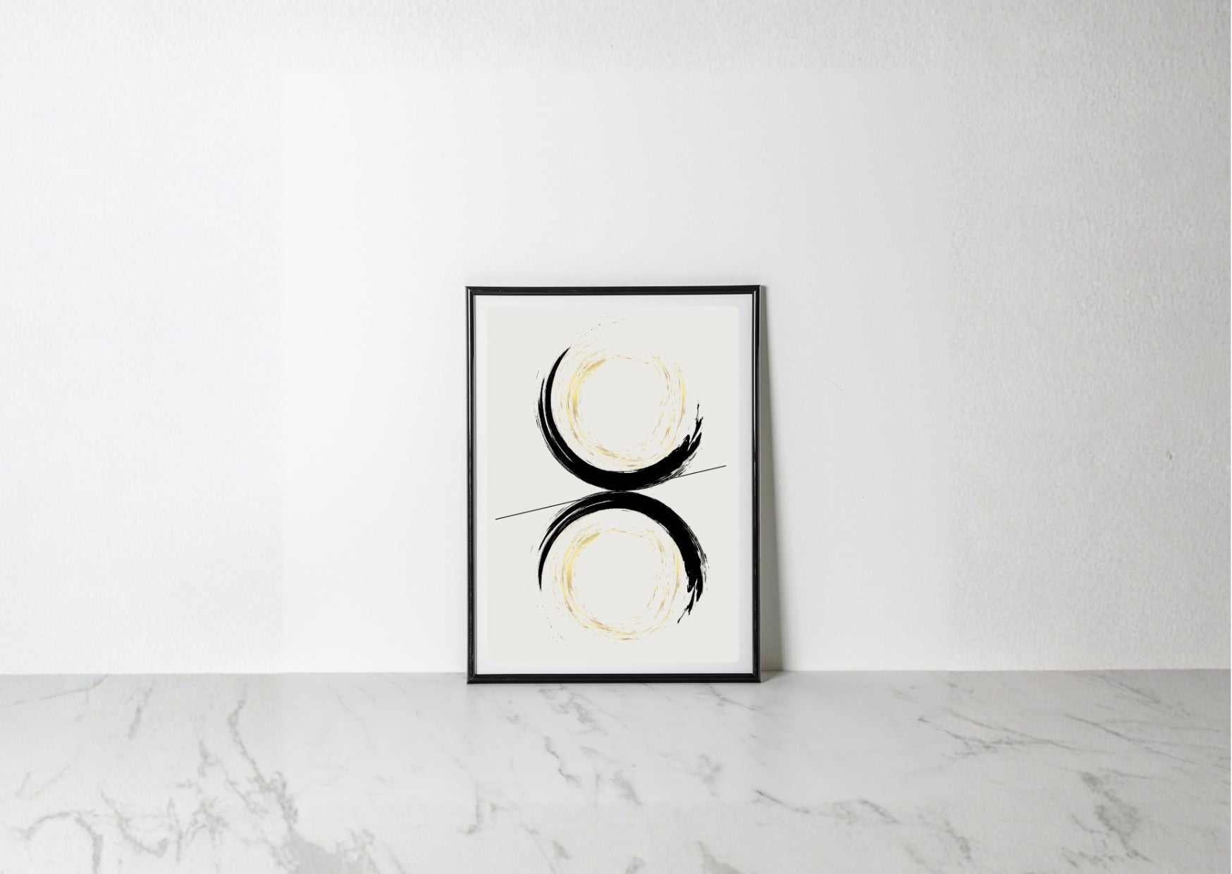 A minimalist framed art print featuring a black and gold abstract circular design on a white background, leaning against a white wall on a light gray marble surface.