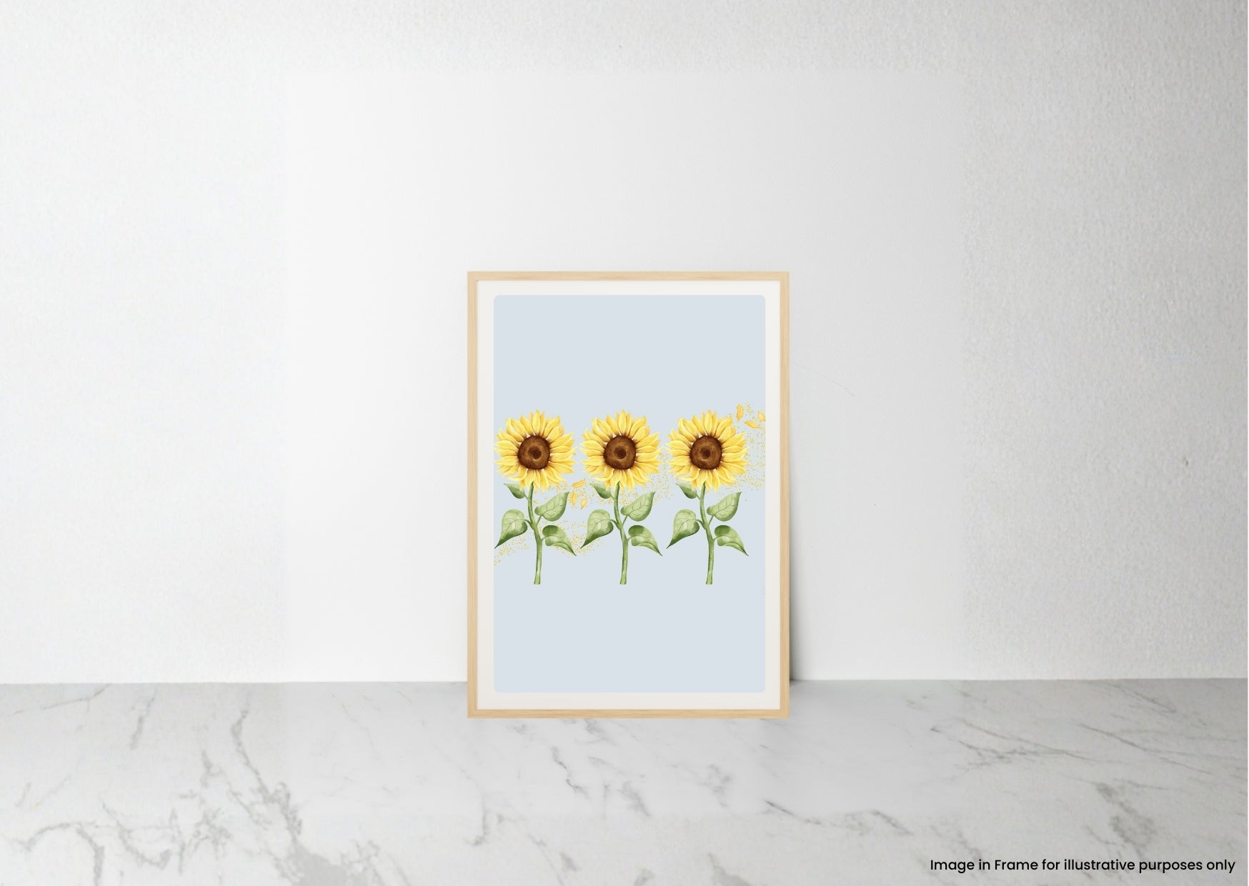 A vertical framed art print featuring three watercolor sunflowers on a pale blue background, leaning against a white wall on a light marble surface.
