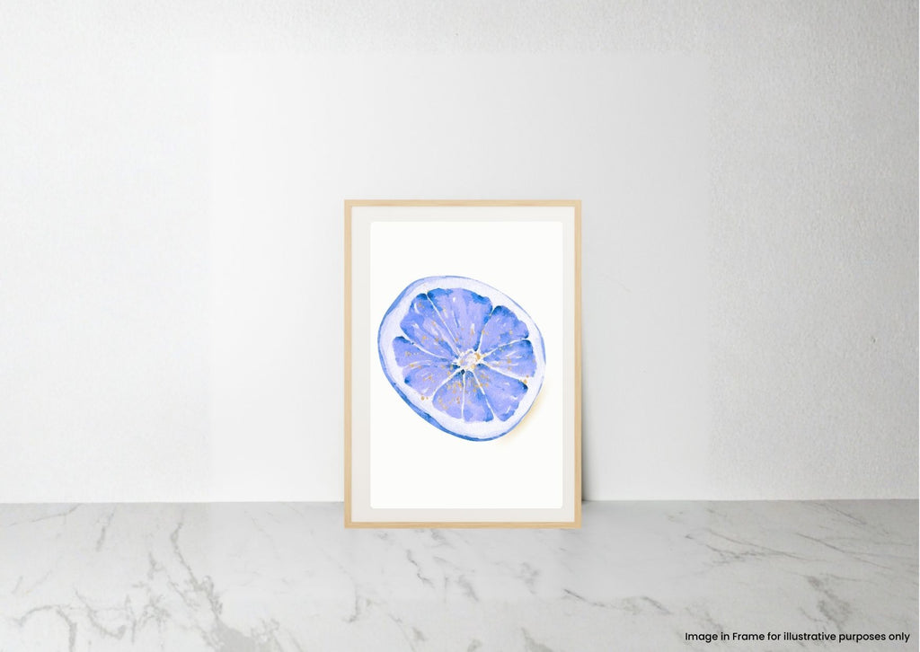 A framed watercolor art print of a blue and purple lemon slice, displayed on a light marble surface against a white wall.
