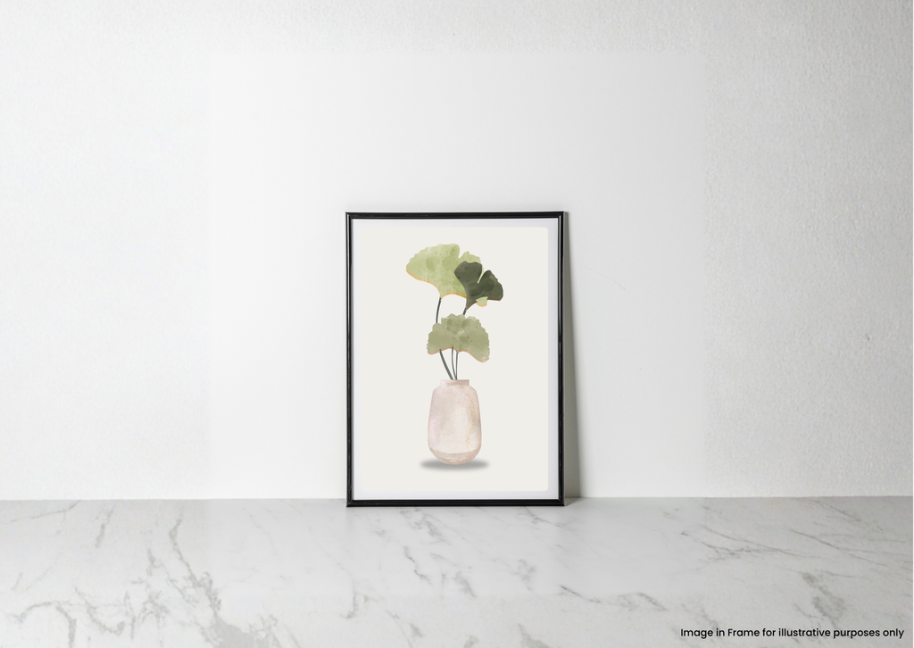 A framed botanical art print featuring green leaves in a pale pink vase, leaning against a white wall on a light marble surface.